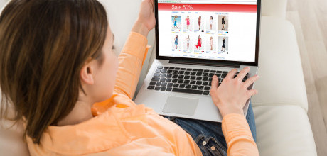 A woman sitting on a couch browsing an online retail site that has a sale