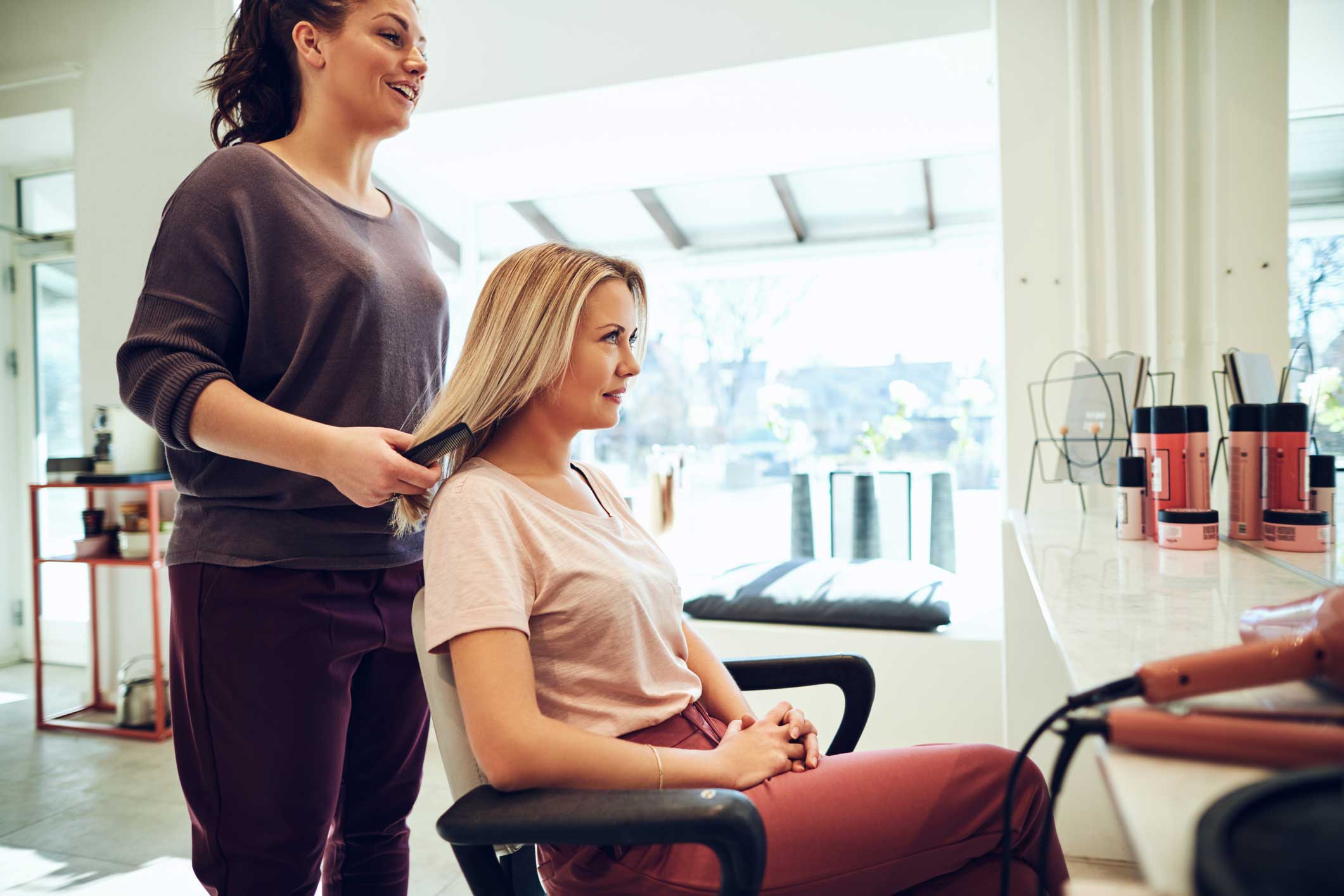 A woman sitting in a salon chair with a hairdresser holding her hair