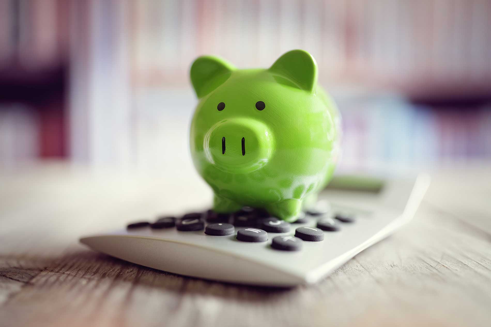 A green piggy bank sitting on a calculator on a desk